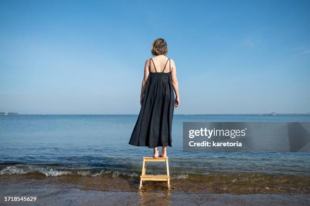 back view of woman standing on stool in sea - ärmelloses kleid stock-fotos und bilder