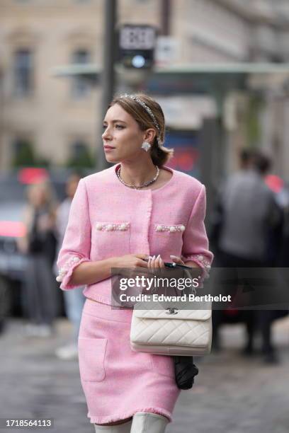 Guest wears a bejeweled headband, earrings, a necklace, a pink full look, a tweed jacket with short sleeves, a mini skirt, a white quilted Chanel...