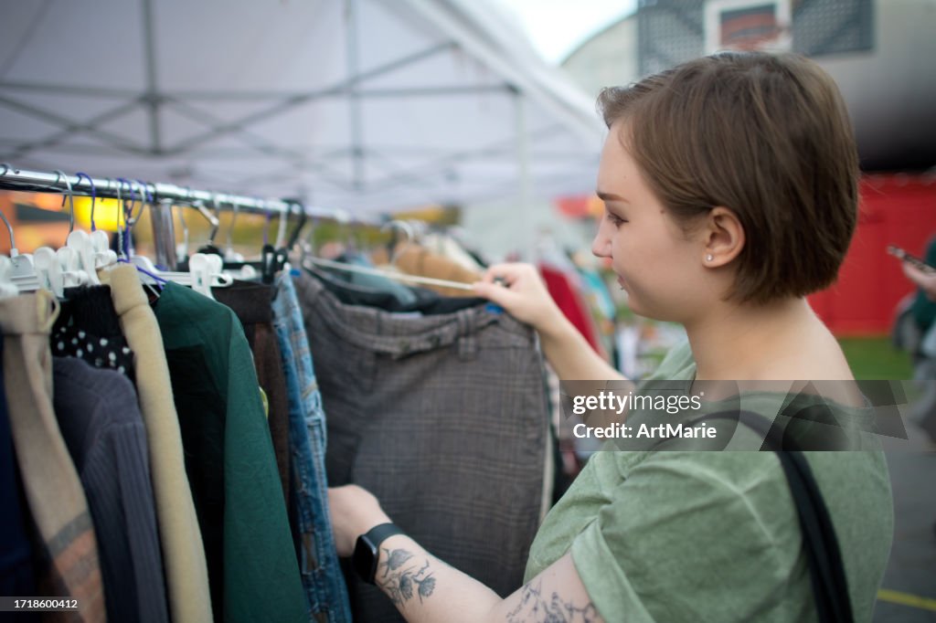 Young woman choosing second hand clothes at a flea market. Zero waste and sustainable lifestyle concept.