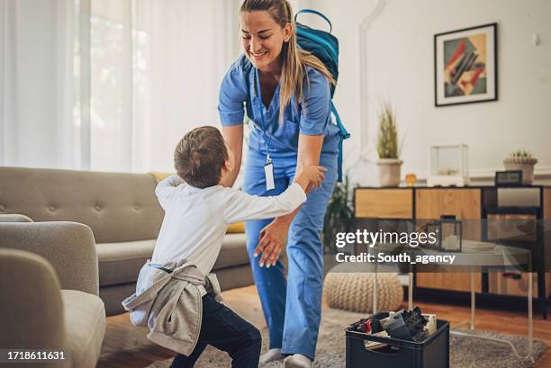 female nurse wearing scrubs playing with her son at home after work - mãe trabalhadora imagens e fotografias de stock