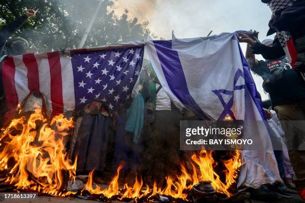 Demonstrators from a pro-Palestinian hardline Muslim group burn a US and Israeli flag during a protest in front of the US embassy in Jakarta on...