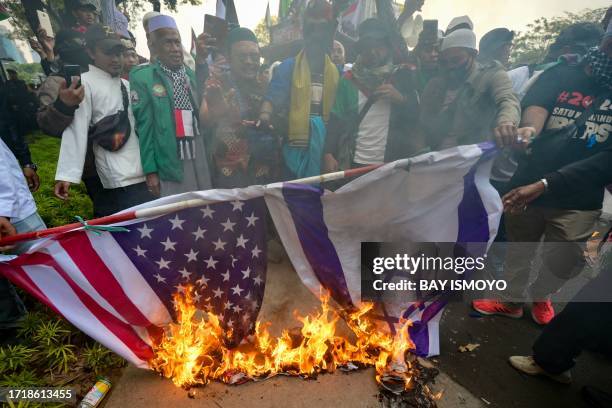 Demonstrators from a pro-Palestinian hardline Muslim group burn a US and Israeli flag during a protest in front of the US embassy in Jakarta on...