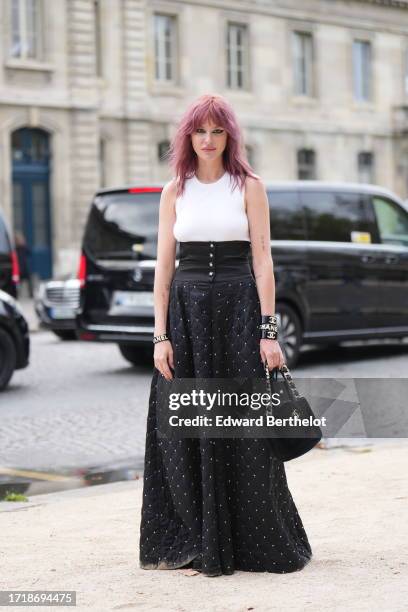 Guest wears a white tank top, a corset, a black quilted long skirt, bracelets, a black fluffy Chanel bag, outside Chanel, during the Womenswear...