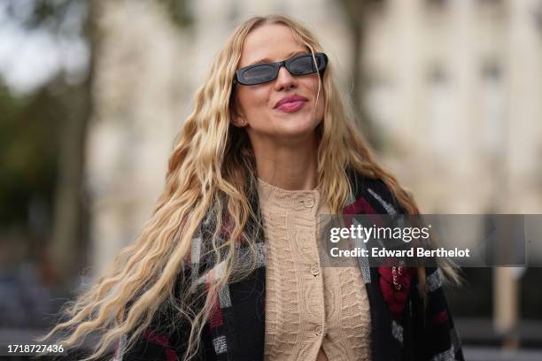 Guest wears sunglasses, a long beige wool cardigan, a gray black and red long jacket, outside Chanel, during the Womenswear Spring/Summer 2024 as...