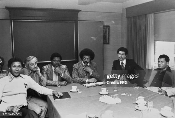 American politician, political activist and Baptist minister Jesse Jackson, adjusting his tie, as he sits among a group of men sitting around a...