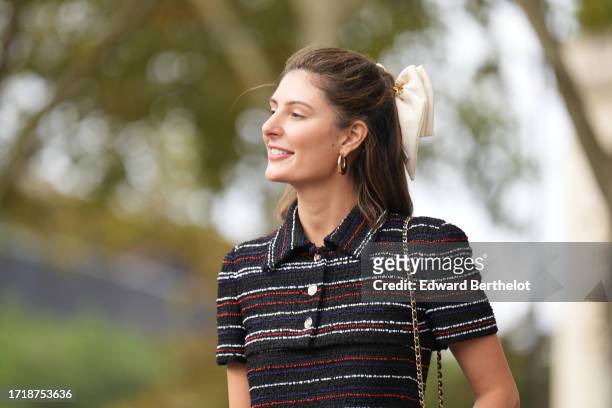 Maria de la Orden wears a bow tie hair bun, golden earrings, a dark blue red and white striped long tweed dress, outside Chanel, during the...