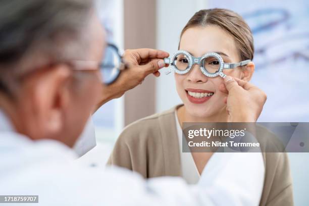 protecting your eyes and overall health by eye experts. a female patient trying on a test glasses frame during eyesight testing with a male optometrist in an ophthalmologist clinic. - presbyopia stock pictures, royalty-free photos & images