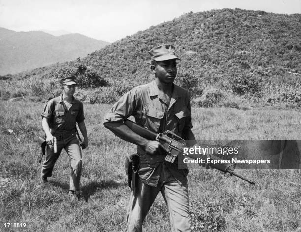 Soldiers Lance Corporal Murphy and Sergeant Paige patrol a jungle area, carrying a rifle and a pistol during the Vietnam War, 1960s.