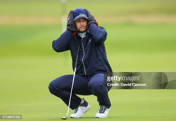 Peter Uihlein of The United States shields his ears from the wind and rain as he prepares to putt on the 16th hole during the first round of the...