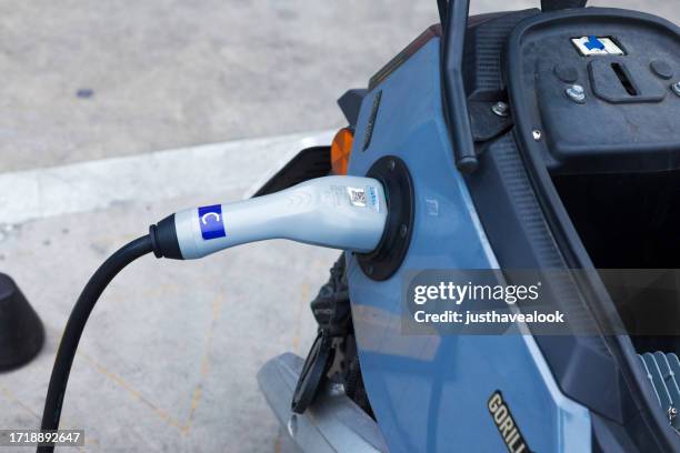 electric motorcycle plugged to ev charger station - lambreta imagens e fotografias de stock