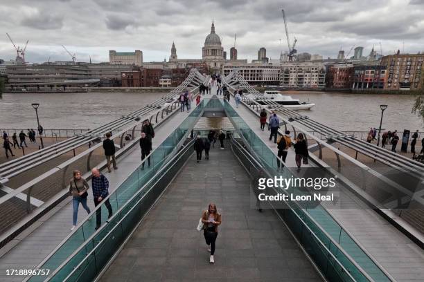 Members of the public walk across the Millennium Bridge on October 05, 2023 in London, England. The pedestrian bridge that spans the River Thames...