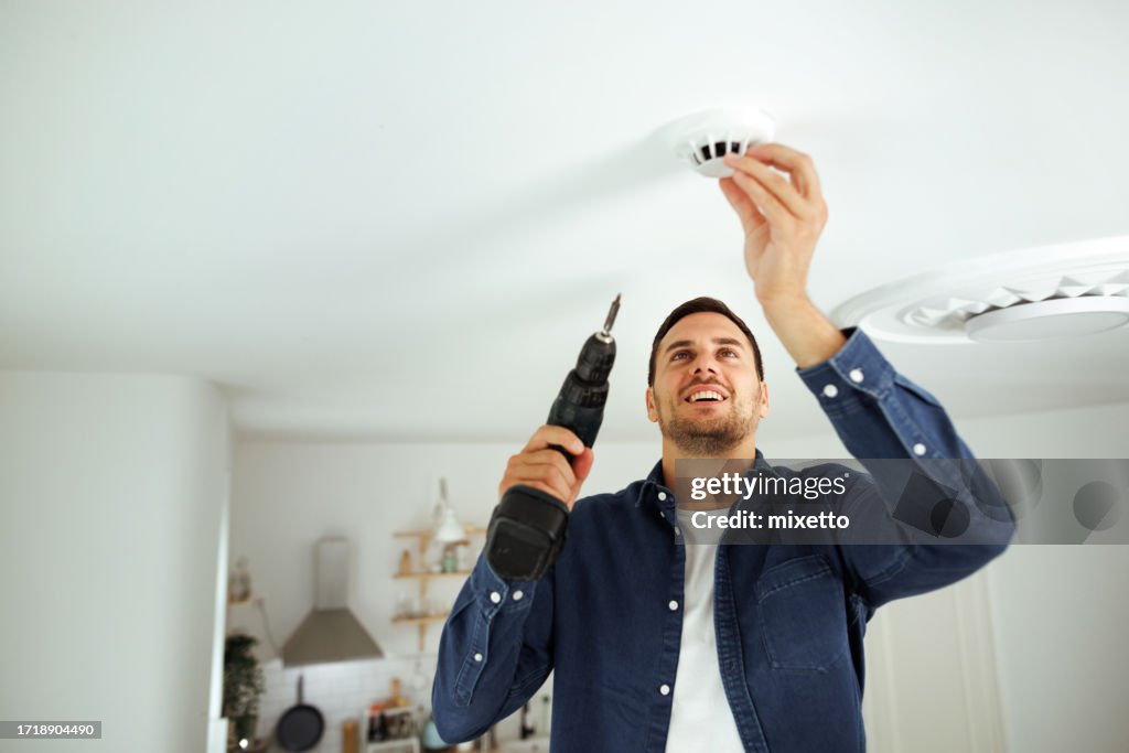 Joven guapo instalando sensor de humo en su casa