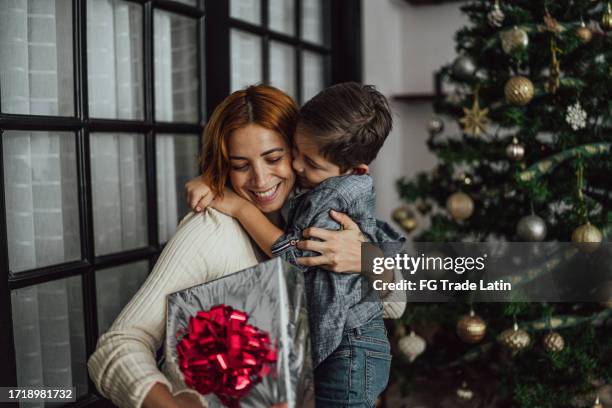 mother giving christmas gifts to son at the home - child hugging tree stock pictures, royalty-free photos & images