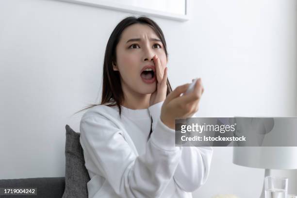 asian woman at home: startled and terrified expression while watching shocking news or horror movie with remote control - film screening room stock pictures, royalty-free photos & images