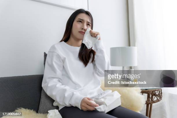 young pretty asian girl sitting on a cozy sofa in the living room and watching tv. - film screening room stock pictures, royalty-free photos & images