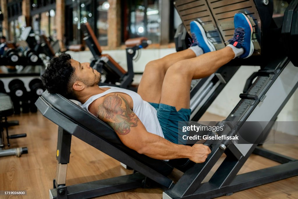 Muscular man exercising on thigh workout machine in gym