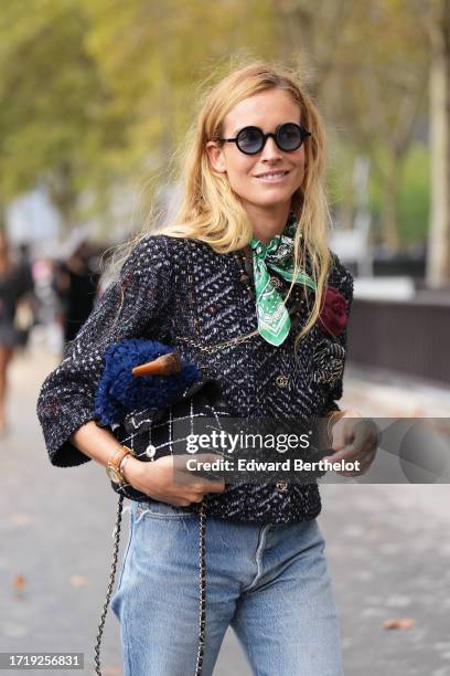 Blanca Miro wears sunglasses, a green scarf, a tweed knit jacket, a black striped Chanel bag, ripped jeans, outside Chanel, during the Womenswear...