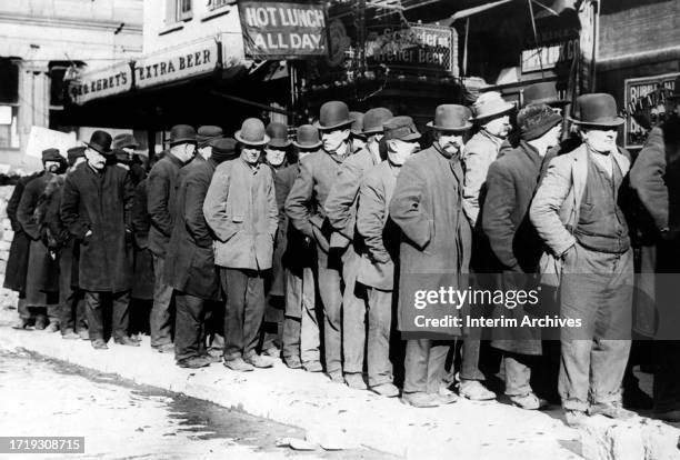 Long line of men form a breadline on the sidewalk at a Bowery establishment, in lower Manhattan, New York, February 7, 1910. A sign above the men...