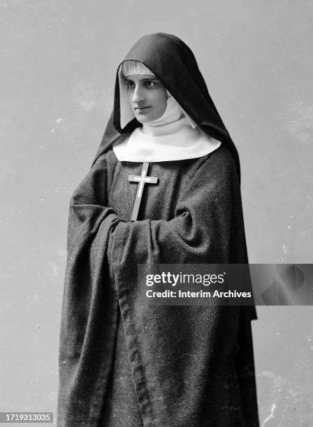 Standing three quarter length portrait of an unidentified nun wearing religious habit, 1900s. Her arms are folded in from of her. Among the parts of...