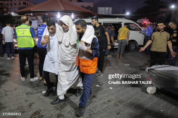 Paramedics help a Palestinian man walk into Al-Shifa hospital in Gaza City during Israeli airstrikes on the Palestinian territory on October 11 as...