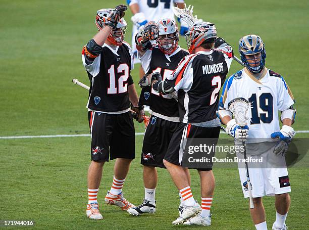 Eric Law celebrates a goal with Justin Turri and Brendan Mundorf of the Denver Outlaws as Kevin Drew of the Charlotte Hounds hangs his head during a...