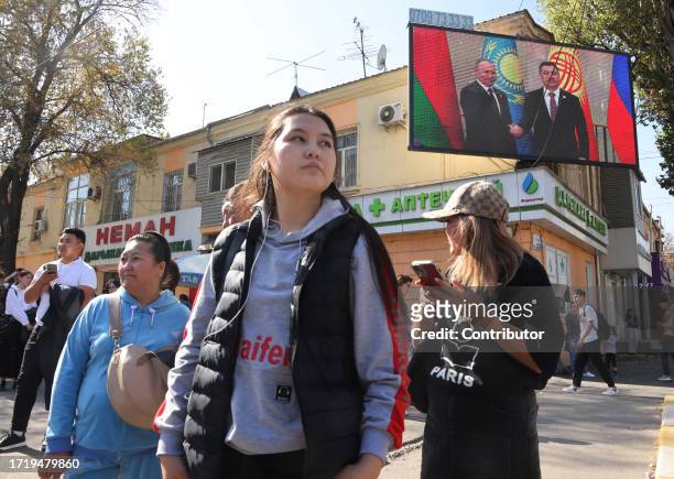 Kyrgyz women walk past to an electronic panel with photo of Russian President Vladimir Putin shaking hands with Kyrgyz President Sadyr Japarov,...