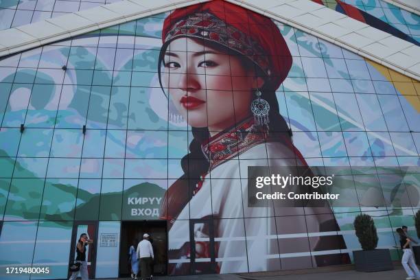 People walk past to the picture of a Kyryz woman above the entrance to the Asia Mall shopping center, October 11 in Bishkek, Kyrgyzstan. Bishkek...