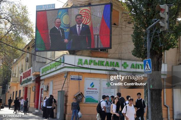 Kyrgyz people walk past to an electronic panel with photo of Russian President Vladimir Putin shaking hands with Kyrgyz President Sadyr Japarov,...