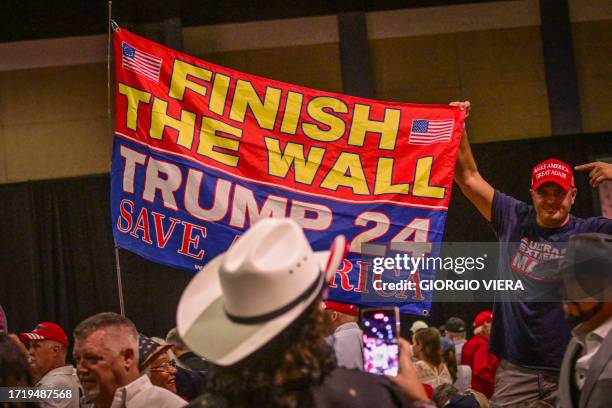 Supporters of former US president and 2024 Republican presidential hopeful Donald Trump hold a sign about the border wall with Mexico before Trump...