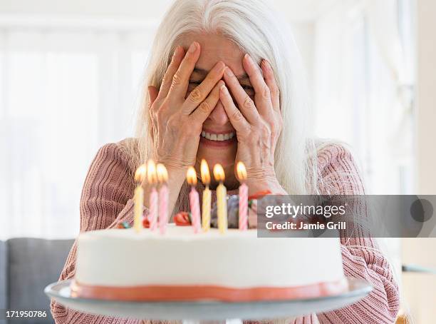 senior woman peeking at candles on birthday cake - dementeren stockfoto's en -beelden