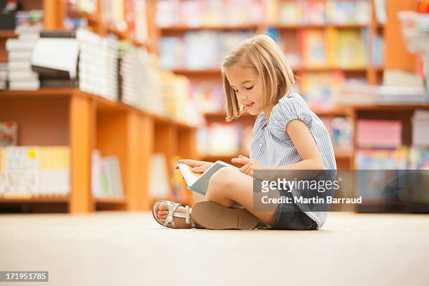 girl sitting on floor of library with book - kids read stockfoto's en -beelden
