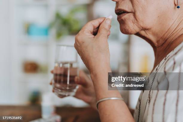senior woman taking medicine at home - tomar remédio imagens e fotografias de stock