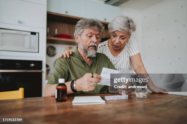 pareja de ancianos medicándose en casa con prescripción médica - medicare fotografías e imágenes de stock