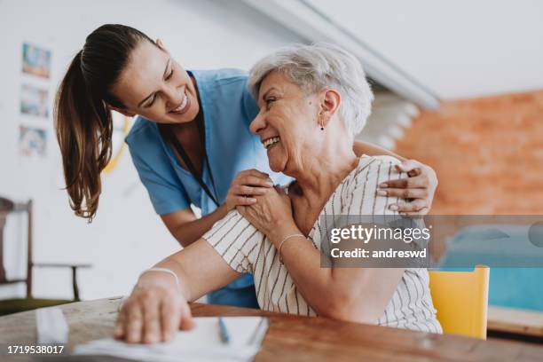 un professionnel de la santé à domicile étreint un patient âgé - infirmière et maison photos et images de collection