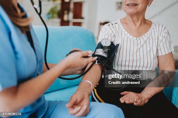 home care healthcare professional measuring blood pressure - bloeddrukmeter stockfoto's en -beelden