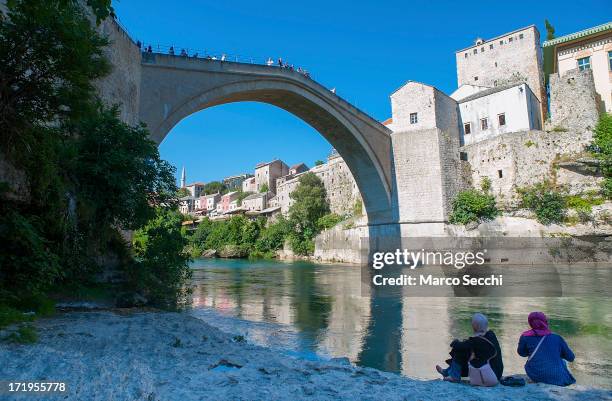 Two Muslim girls sit on the bank of the Neretva river under the Old Bridge as the city of Mostar remembers the 1993 conflict on June 28, 2013 in...