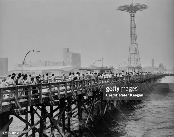 People crabbing, dangling crab lines off a pier, with the Parachute Jump ride in the background, at Coney Island in the borough of Brooklyn, New York...