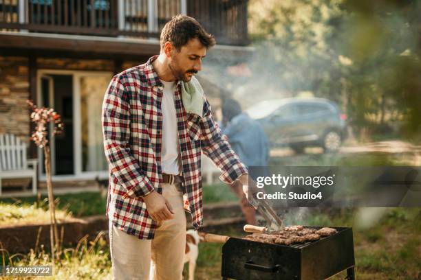 capturing the essence of summer, a man stands proudly by his grill, creating a backyard barbecue masterpiece - masterpiece midsummer party stock pictures, royalty-free photos & images