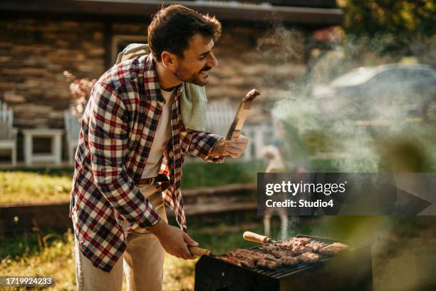 capturing the essence of summer, a man stands proudly by his grill, creating a backyard barbecue masterpiece - masterpiece midsummer party stock pictures, royalty-free photos & images