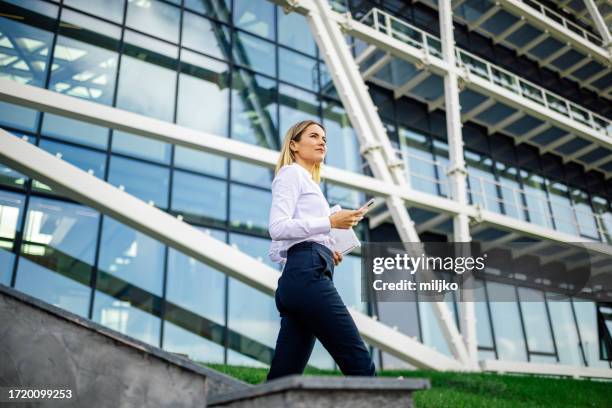 young business woman is walking in front of modern office building and using mobile phone - in front of stock pictures, royalty-free photos & images