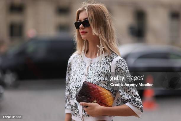 Xenia Adonts is seen outside Chanel show wearing black Chanel sunnies, Chanel pearl earrings, Chanel sequin crystal shiny cardigan, Chanel wide leg...