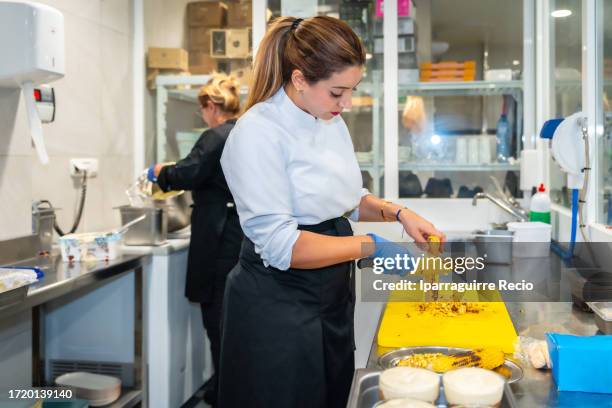 female chef cutting fried corn on the cob in restaurant kitchen interior - kokkin stockfoto's en -beelden