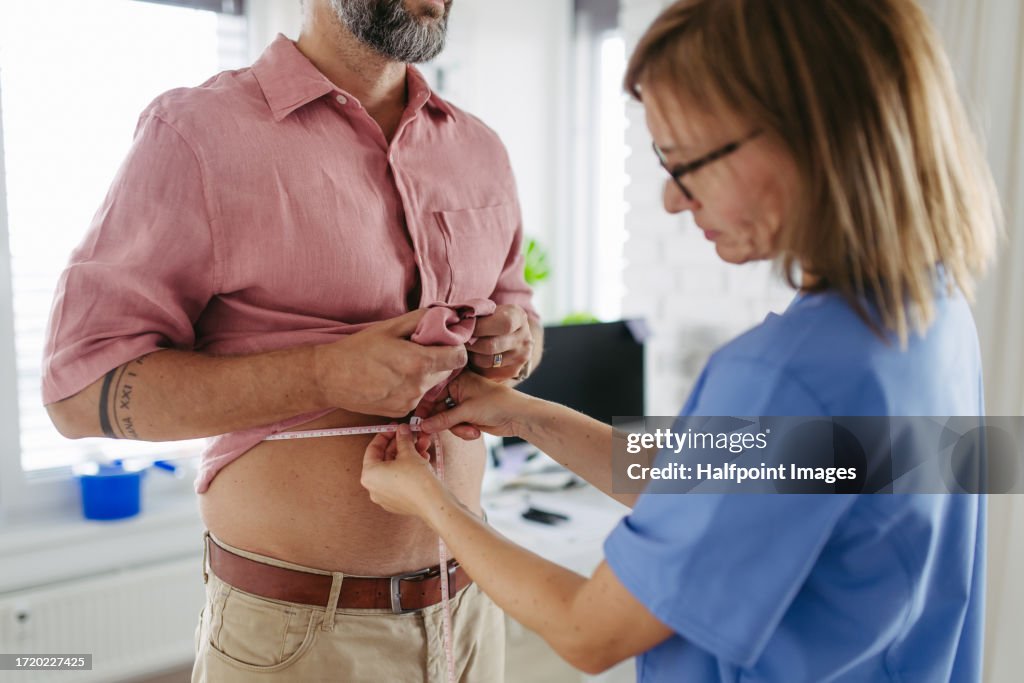 Diabetologist doctor measuring patient’s waist, examine abdominal obesity in diabetes clinic.