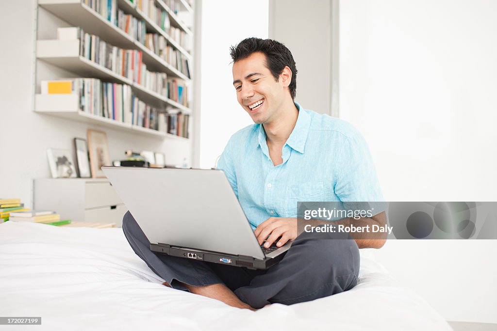 Hombre sentado en la cama con la computadora portátil