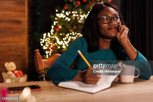 young woman contemplating her new year's resolutions and writing them in a diary - woman planning stock pictures, royalty-free photos & images