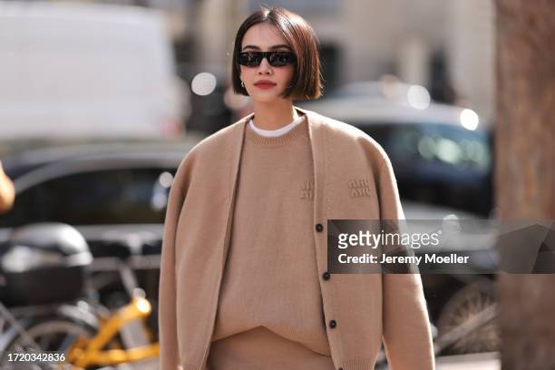 Fashion Week Guest is seen wearing a white T-shirt, a beige sweater by Miu Miu, a beige knit jacket by Miu Miu, a beige knit skirt, silver creoles,...