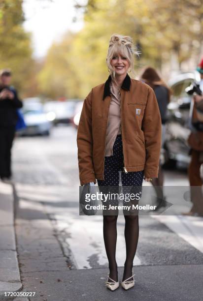 Emili Sindlev is seen wearing a beige cardigan, with a brown jacket from Carhartt, dark blue shorts with white dots, a gray Miu Miu Hobo handbag,...