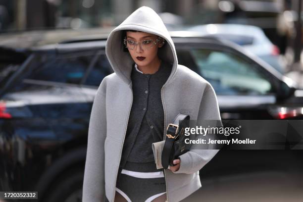 Kiwi Lee Han is seen wearing a grey top, a grey cardigan, a light grey oversized hooded jacket, white and grey shorts, a black leather handbag and...