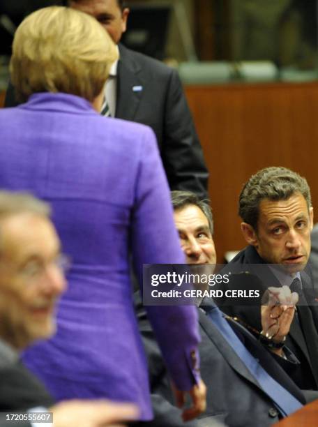 French President Nicolas Sarkozy and French Prime Minister Francois Fillon look at German Chancellor Angela Merkel attend a working session of an EU...