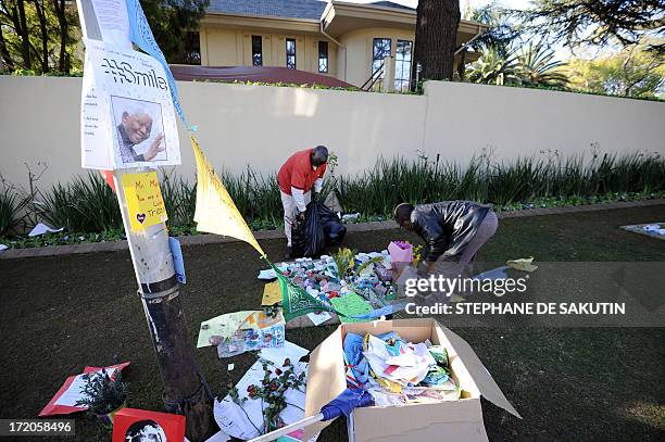 Housekeeper removes flowers and well wishing messages left for former South African President Nelson Mandela outside his house on July 1, 2013 in...